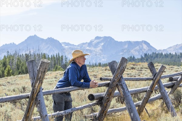 Man leaning on wooden fence by mountains in Stanley, Idaho, USA