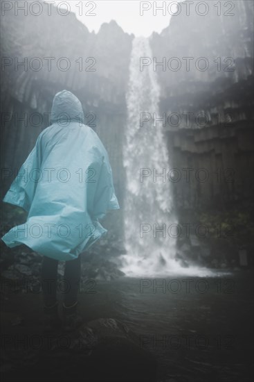 Woman wearing blue raincoat by waterfall in Skaftafell, Iceland