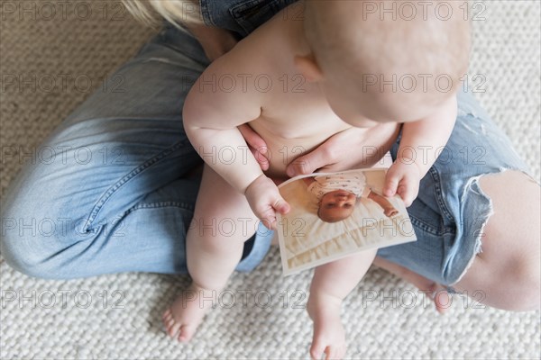 Baby girl holding photograph in her mother's lap