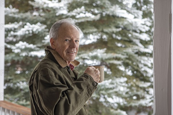 Senior man with cup of coffee by snowy pine tree