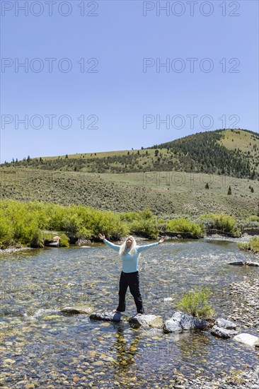 USA, Idaho, Sun Valley, Woman with arms raised standing on rocks in river