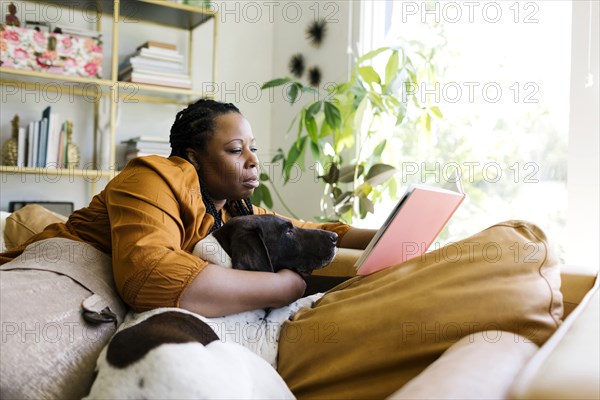 Woman reading book on sofa with her dog