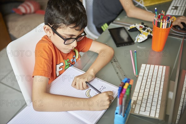 Boys (8-9) writing in notebook while learning at home during Covid-19 lockdown