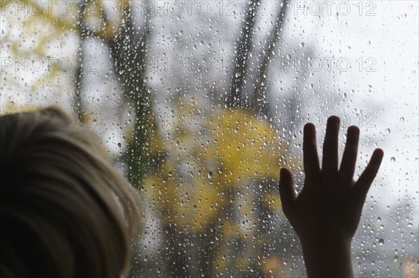 Close-up of boy (6-7) looking through window on rainy day