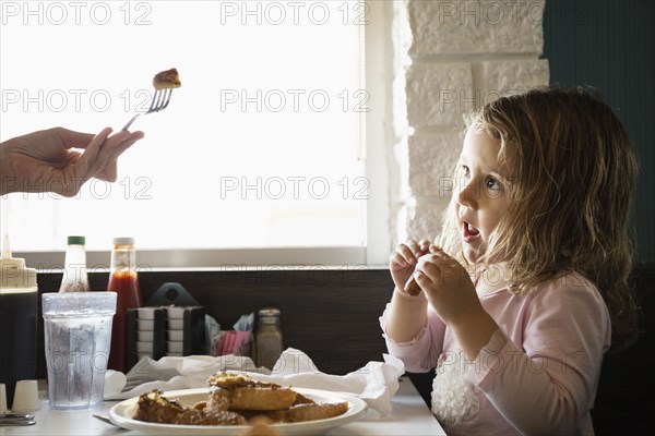 Hand of mother feeding toddler daughter in diner