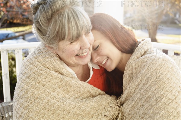Senior woman and adult daughter wrapped in a blanket on porch