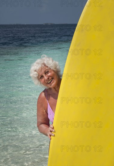 Older Caucasian woman holding surfboard on beach