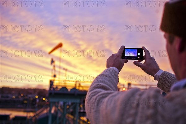 Man taking picture of sunset over bridge