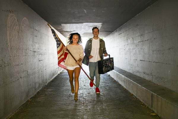 Caucasian couple carrying American flag and boom box in tunnel