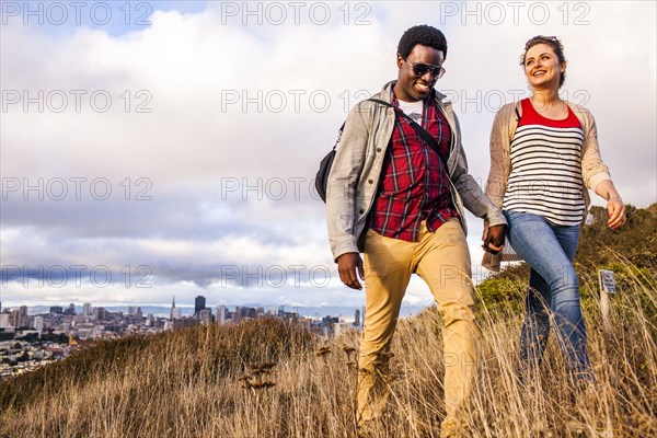 Couple walking on grassy hill overlooking cityscape