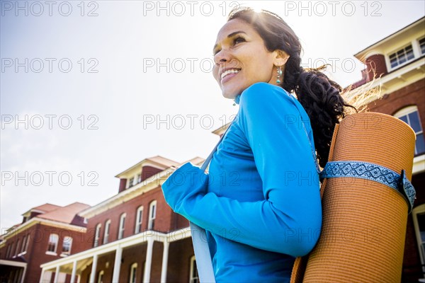 Hispanic woman carrying yoga mat outdoors