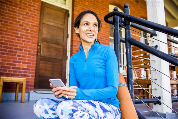 Hispanic woman using cell phone on porch