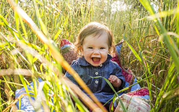 Caucasian baby girl sitting in tall grass