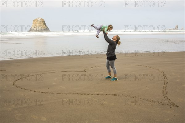 Caucasian mother lifting daughter in heart-shape on beach