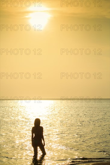 Silhouette of Mixed Race woman wading in ocean at sunset