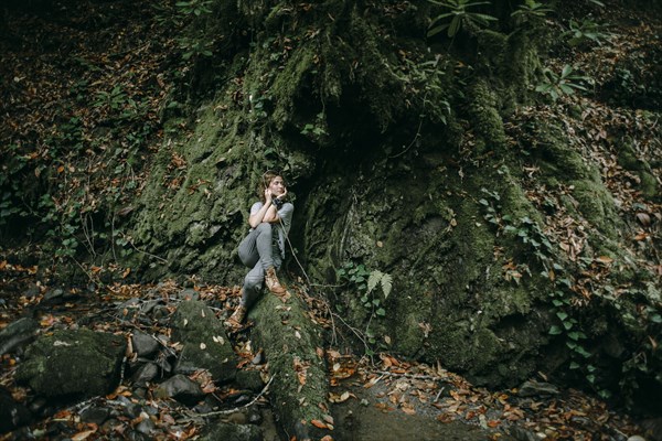 Caucasian woman sitting in forest holding branch