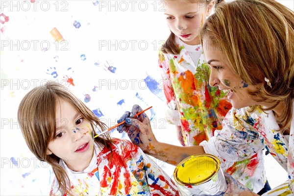 Messy Hispanic mother painting daughter's face