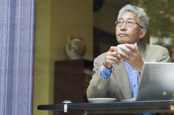Senior Asian businessman with laptop at cafe