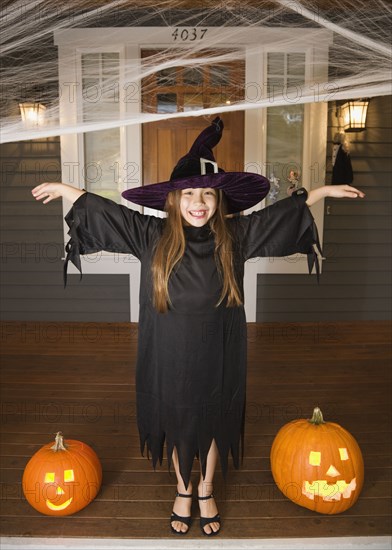 Mixed race young girl in witch costume with Halloween pumpkins