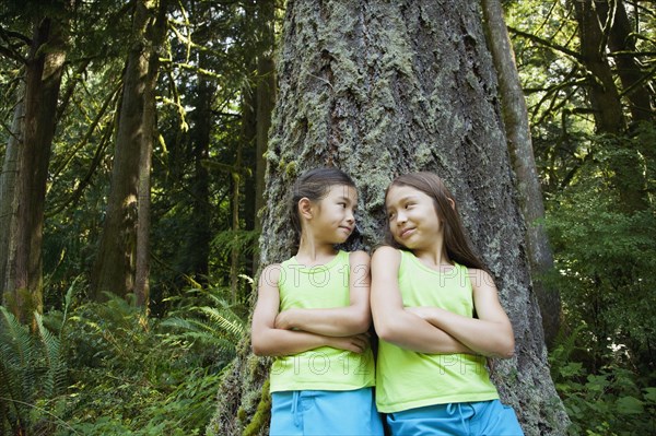 Mixed race girls leaning on tree