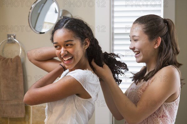 Teenage girls styling hair in bathroom mirror