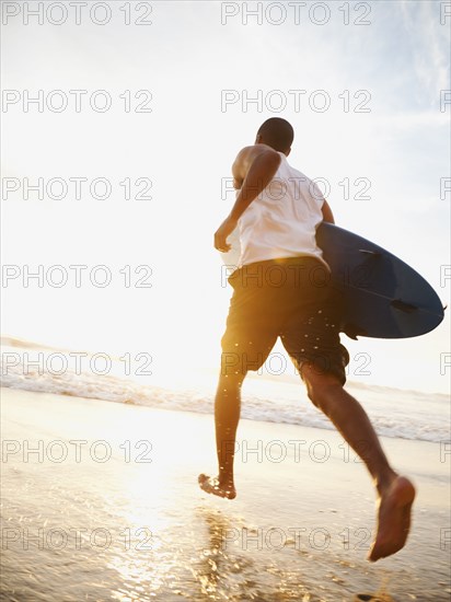 Black man running with surfboard on beach