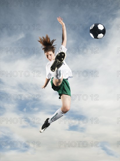 Caucasian teenager kicking soccer ball in mid-air