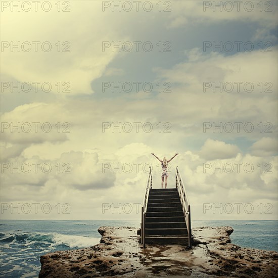 Caucasian woman on stairs on rocks next to ocean