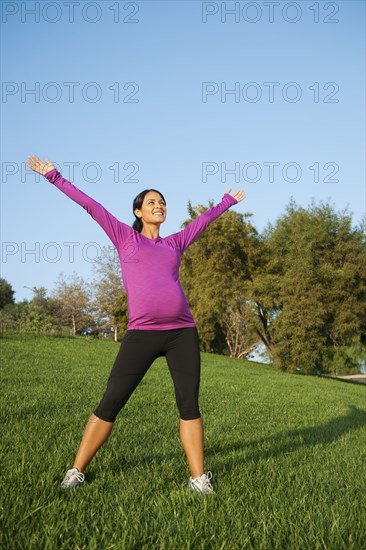 Pregnant Hispanic woman stretching outdoors