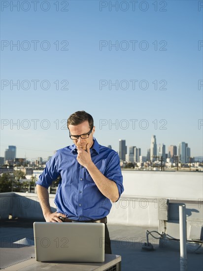 Caucasian businessman using laptop on urban rooftop