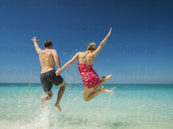 Caucasian couple jumping for joy in tropical ocean