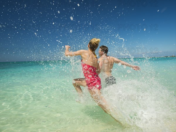 Caucasian couple splashing in waves in tropical ocean
