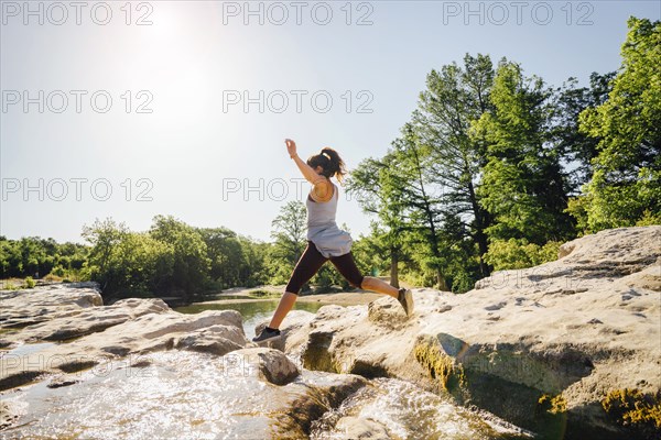 Caucasian woman jumping on rocks near river