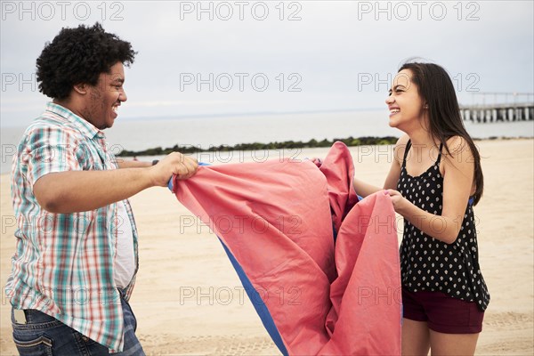 Laughing couple holding blanket on beach