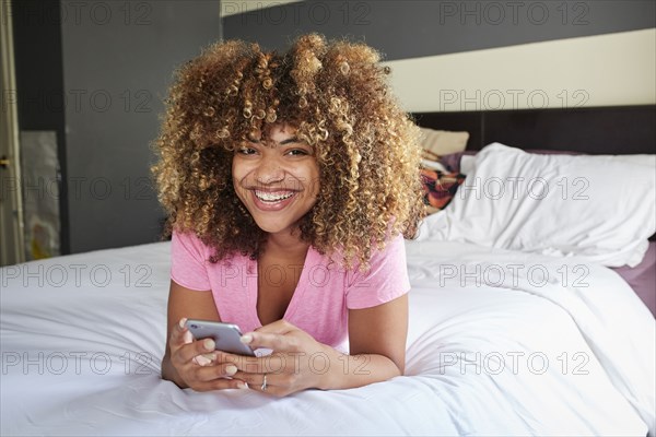 Smiling Black woman laying on bed texting on cell phone