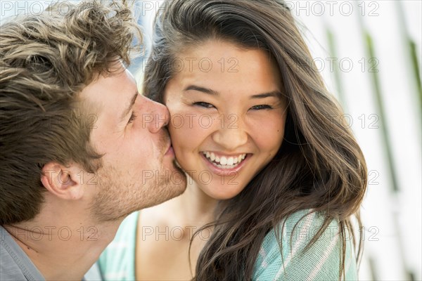 Man kissing girlfriend's cheek outdoors