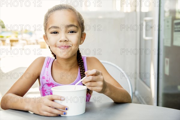 Mixed race girl eating ice cream at outdoor cafe