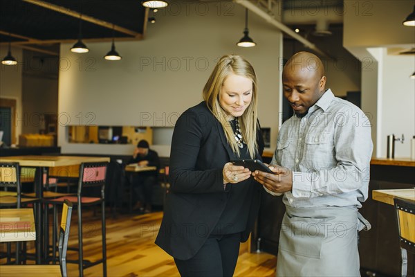 Waiter and businesswoman using cell phones in cafe