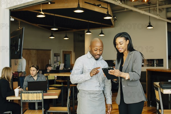 Waiter and businesswoman using digital tablet in cafe