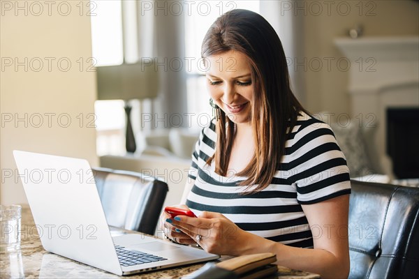 Hispanic woman using laptop and cell phone
