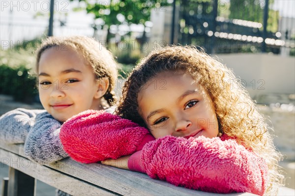 Mixed Race sisters leaning on wooden railing