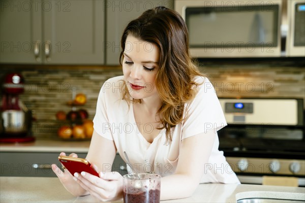 Woman texting on cell phone in domestic kitchen
