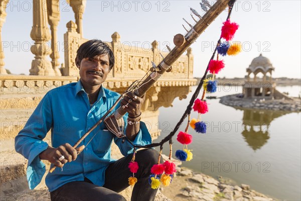 Indian man holding traditional instrument near monument