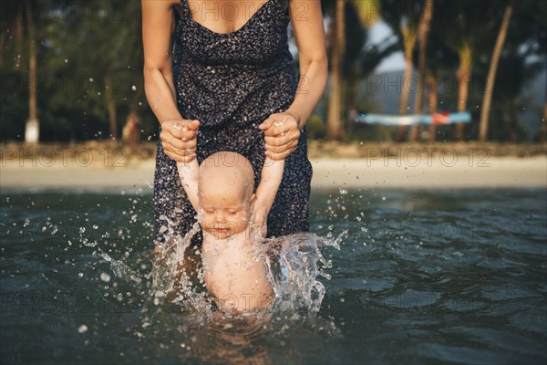Caucasian mother holding arms of baby daughter splashing in ocean