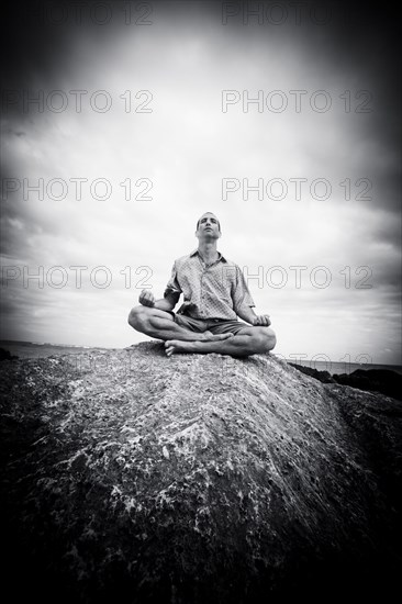 Caucasian man meditating on rocks at ocean