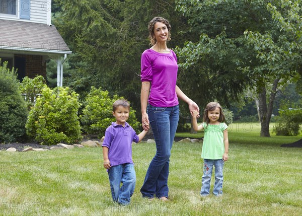 Mother holding hands with son and daughter in front yard