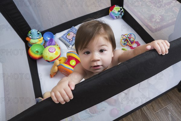 Mixed race baby girl standing in playpen