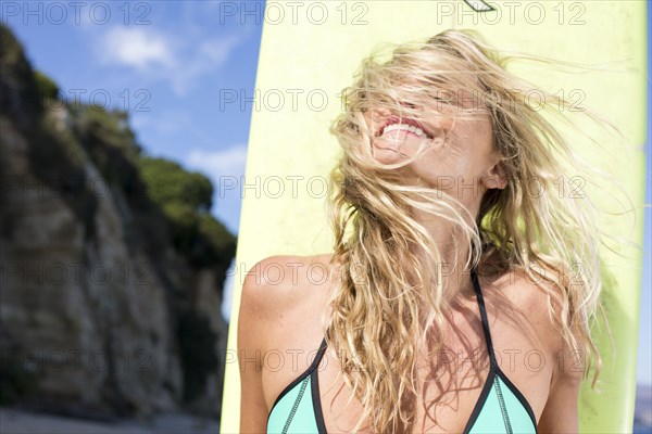 Wind blowing hair of Caucasian woman holding surfboard