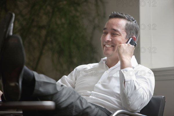 Mixed race businessman with feet on desk using cell phone