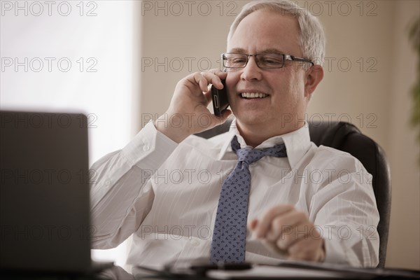 Caucasian businessman talking on cell phone at desk